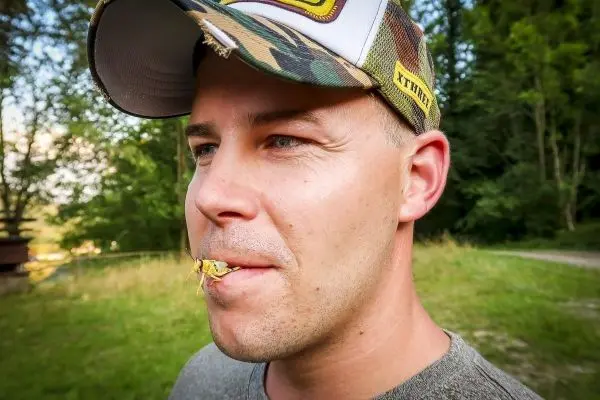 Mann mit einer Heuschrecke im Mund steht in einer grünen Umgebung