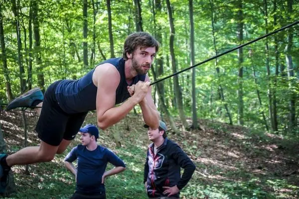 Mann überquert selbstgebaute Seilbrücke, während andere zuschauen
