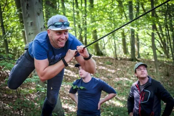 Mann überquert selbstgebaute Seilbrücke, während andere zuschauen
