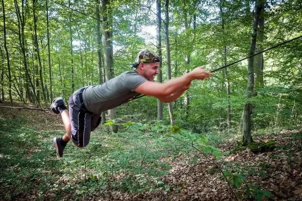 Mann überquert selbstgebaute Seilbrücke zwischen Bäumen im Wald