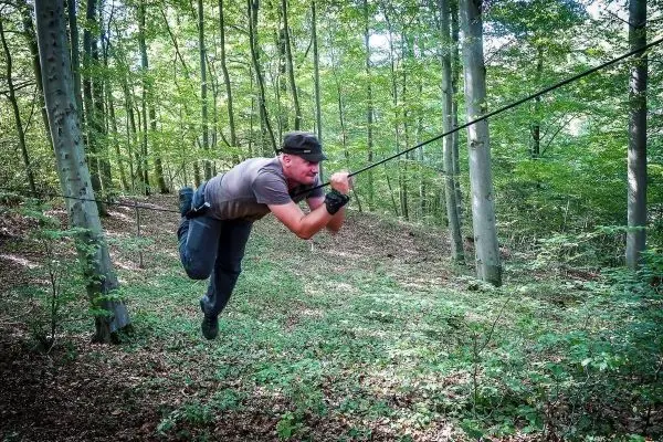 Mann überquert selbstgebaute Seilbrücke zwischen Bäumen im Wald