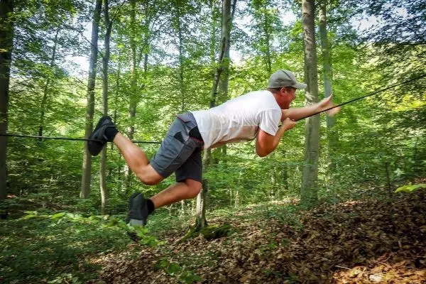 Mann überquert selbstgebaute Seilbrücke zwischen Bäumen im Wald