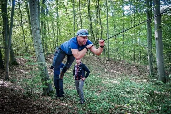 Mann überquert selbstgebaute Seilbrücke zwischen Bäumen im Wald