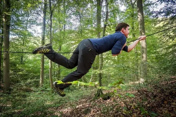 Mann überquert selbstgebaute Seilbrücke zwischen Bäumen im Wald
