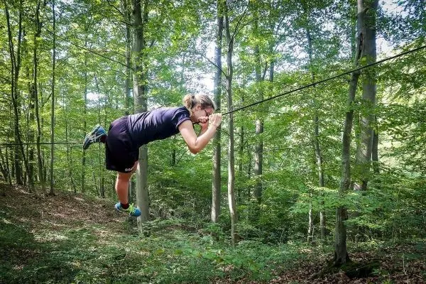 Person schwingt sich an einer selbstgebauten Seilbrücke durch den Wald