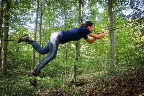 Person überquert selbstgebaute Seilbrücke im Wald beim Survival Training
