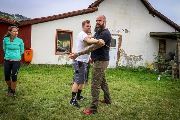 Zwei Personen üben eine Selbstverteidigungstechnik im Freien, während eine dritte Person zuschaut