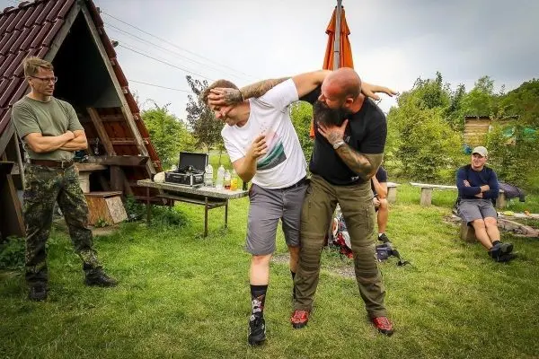 Zwei Personen üben eine Selbstverteidigungstechnik im Freien, während Zuschauer beobachten