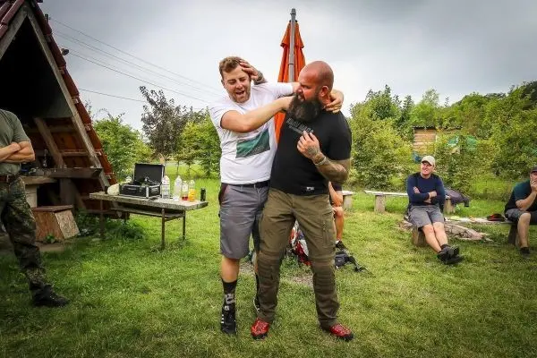 Zwei Personen üben eine Selbstverteidigungstechnik im Freien, Zuschauer im Hintergrund