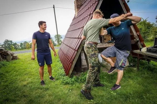 Zwei Personen üben eine Selbstverteidigungstechnik vor einer kleinen Hütte