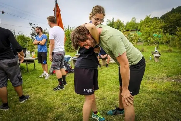 Zwei Personen üben eine Trage-Technik im Freien, umgeben von weiteren Teilnehmern
