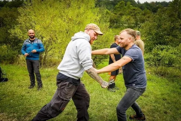 Zwei Personen üben einen körperlichen Griff im Freien, umgeben von anderen Teilnehmern