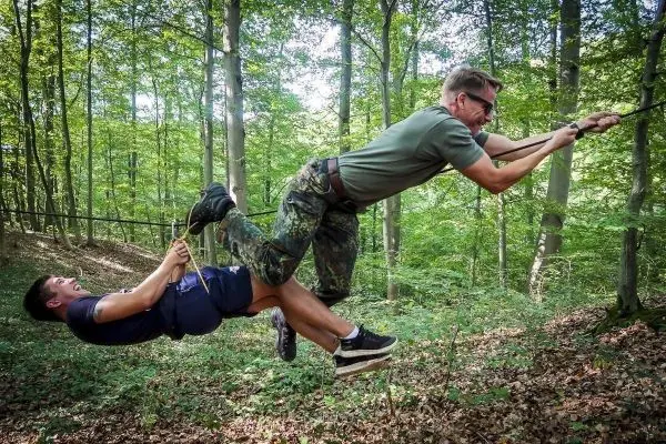 Zwei Personen überqueren eine selbstgebaute Seilbrücke im Wald
