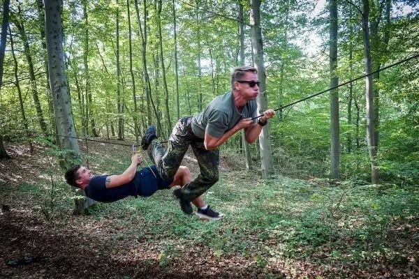 Zwei Personen überqueren eine selbstgebaute Seilbrücke im Wald