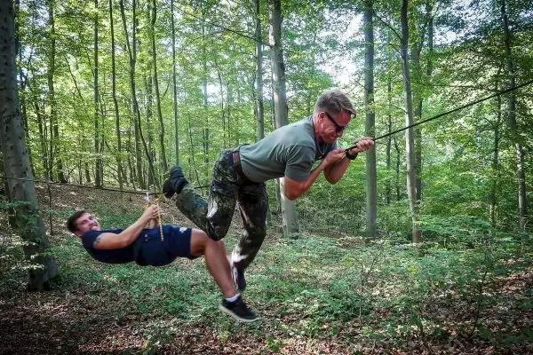 Zwei Personen überqueren eine selbstgebaute Seilbrücke im Wald