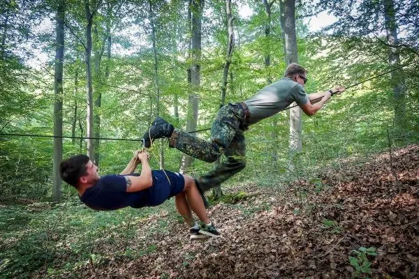 Zwei Personen überqueren eine selbstgebaute Seilquerung im Wald