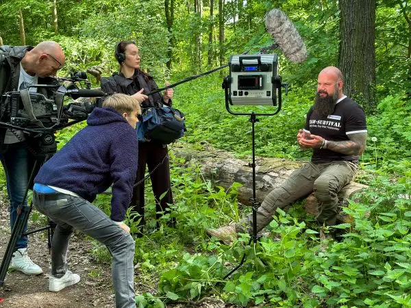 Dreharbeiten im Wald mit Kamera, Mikrofon und Interviewpartner auf Baumstamm