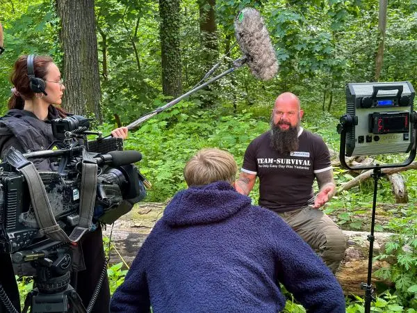 Drei Personen filmen ein Interview im Wald mit Kamera und Mikrofon