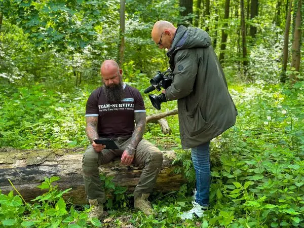 Mann sitzt auf Baumstamm und betrachtet Tablet, während ein Fotograf ihn aufnimmt