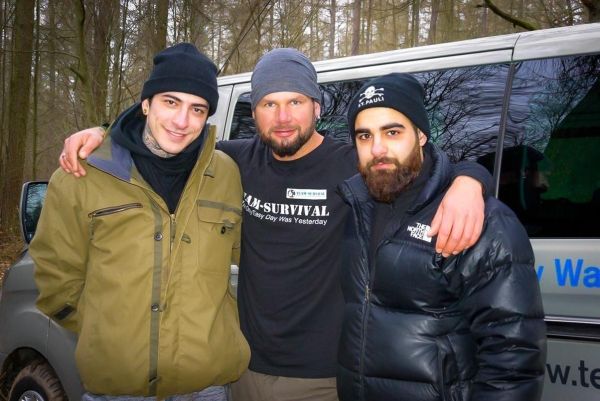 Drei Personen stehen vor einem Fahrzeug im Wald und lächeln