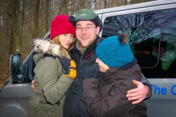 Drei Personen umarmen sich vor einem Fahrzeug im Wald