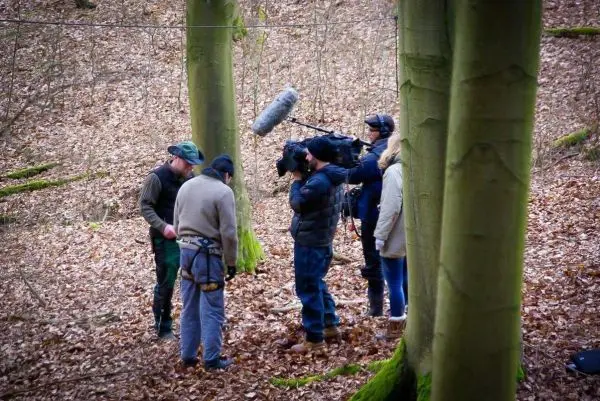 Gruppe filmt im Wald mit Kamera und Mikrofon, während sie sich um einen Tisch versammeln
