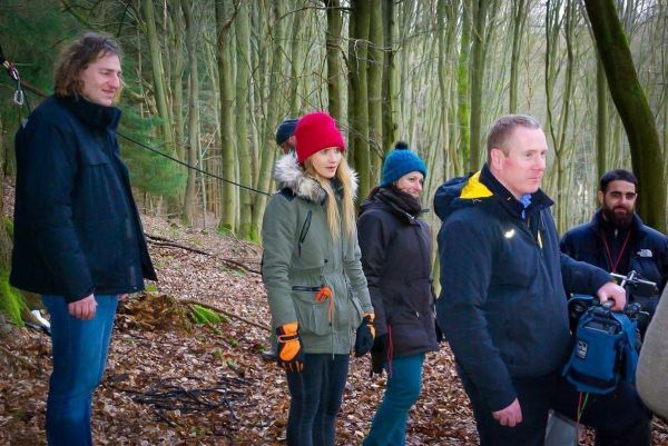 Gruppe steht im Wald auf Laub, einige halten Ausrüstung in den Händen