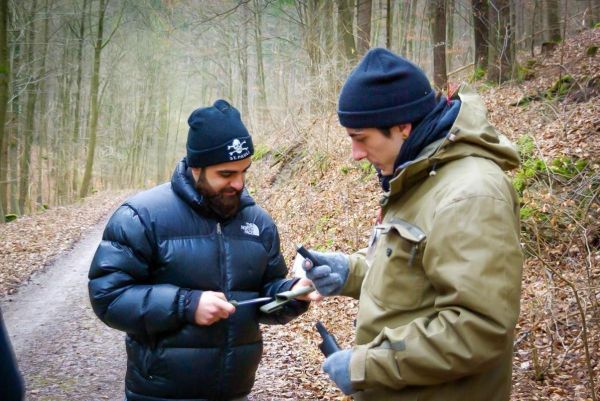 Zwei Personen betrachten ein Messer auf einem Waldweg zwischen Bäumen