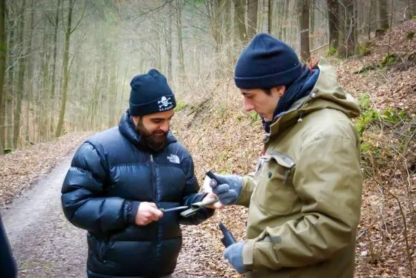 Zwei Personen betrachten ein Messer auf einem Waldweg zwischen Bäumen