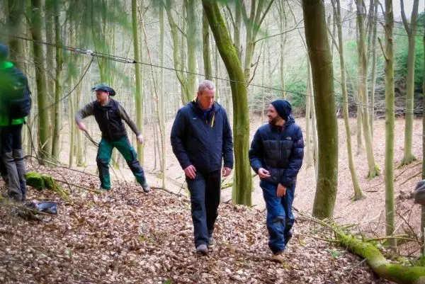 Zwei Personen gehen auf Laubboden, im Hintergrund eine Seilquerung sichtbar