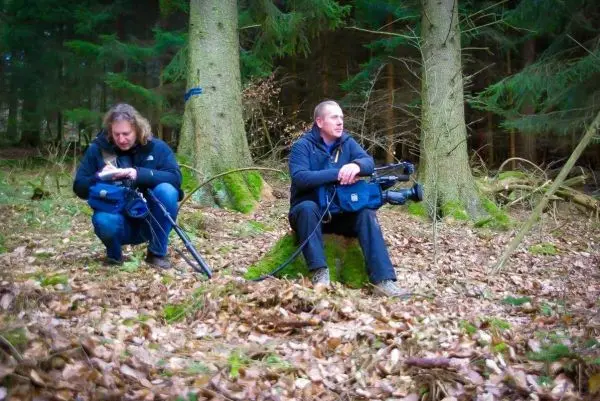 Zwei Personen sitzen auf dem Boden im Wald und halten Kameras