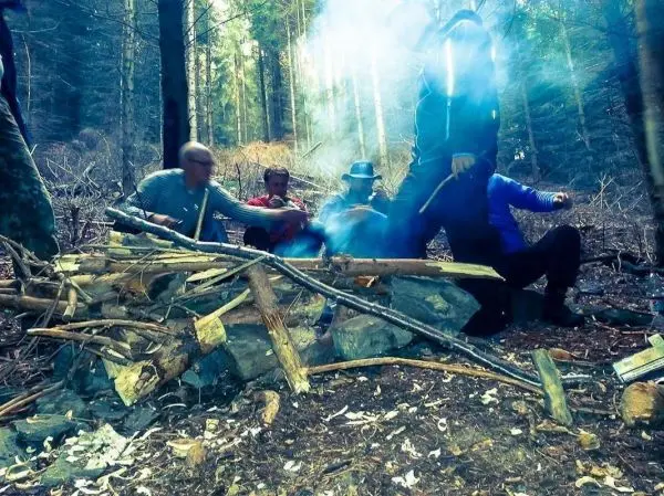 Gruppe sitzt um ein Feuer und arbeitet mit Holzstücken beim Überlebenstraining