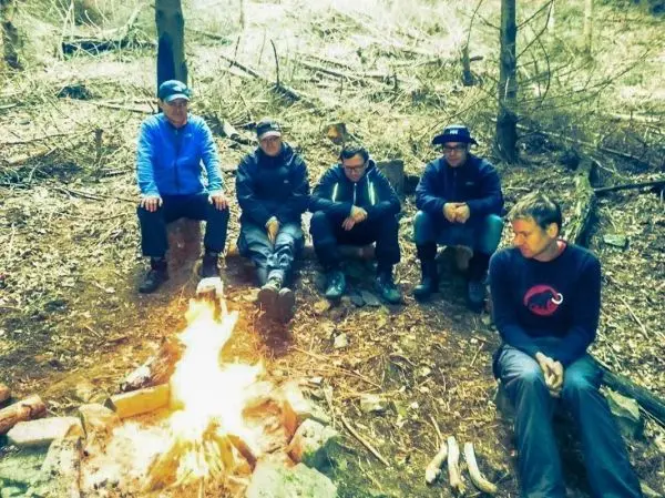 Kleine Flamme brennt im Lagerfeuer, fünf Personen sitzen davor