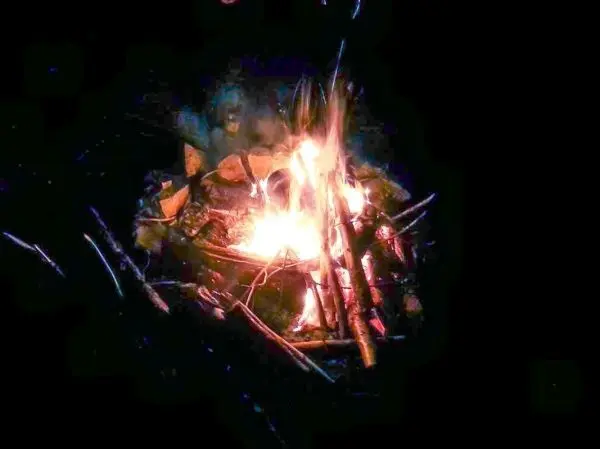 Kleine Flamme mit Rauch und glühenden Holzstücken im Feuer