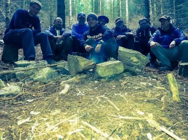 Lagerfeuer zwischen Steinen in einem Wald, Teilnehmer sitzen im Halbkreis