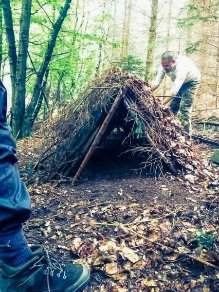 Mann baut eine Tarp-Notunterkunft aus Ästen und Laub im Wald
