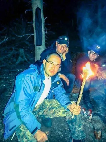 Mann hält brennenden Stock in der Hand, während andere am Lagerfeuer sitzen