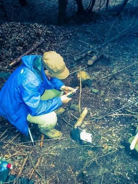 Mann sitzt auf dem Boden und nutzt ein Smartphone in einem Waldgebiet