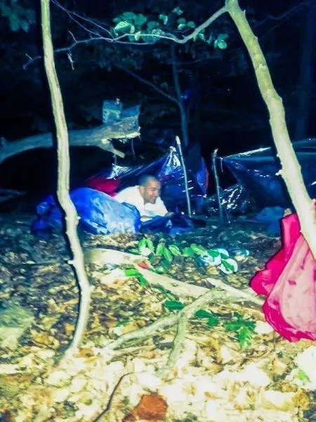 Mann sitzt in einer improvisierten Unterkunft aus Planen im Wald