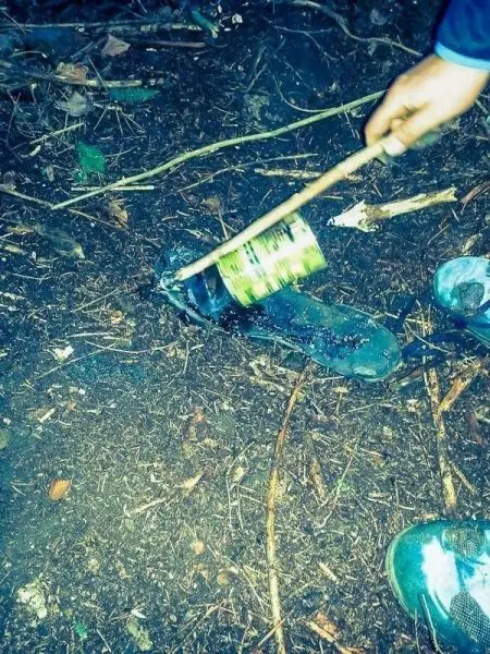 Person hält Stock über einem Kochtopf im Wald