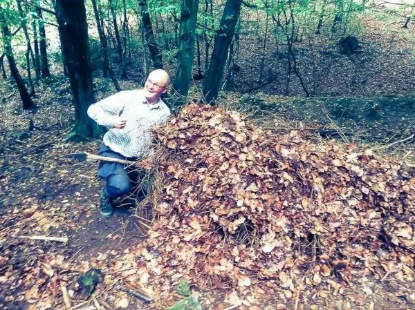 Person zeigt auf einen Haufen aus Blättern und Ästen im Wald