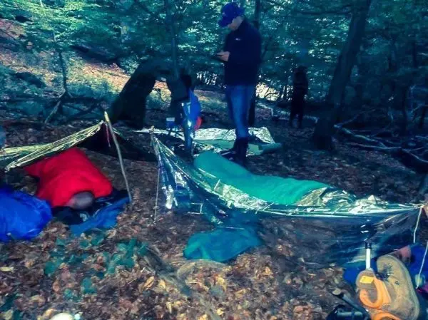 Tarp-Notunterkünfte aus reflektierendem Material im Wald, Personen in Schlafsäcken