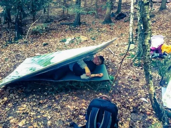 Tarp-Notunterkunft schützt vor Regen, Person liegt auf Isomatte darunter
