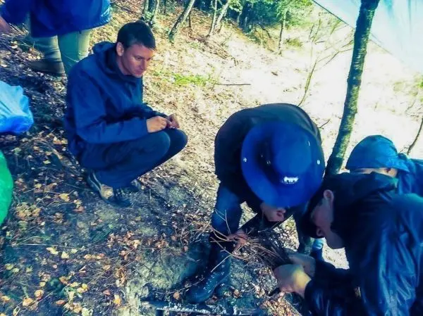 Zwei Personen bereiten Zunder aus Ästen für ein kleines Bodenfeuer vor