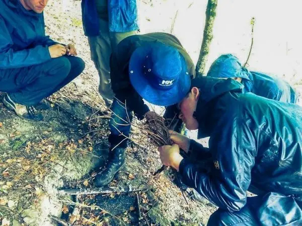 Zwei Personen bündeln Äste zum Zunder, während andere beobachten