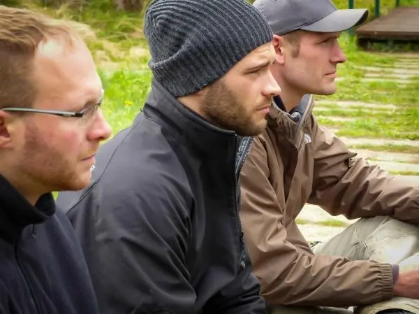 Drei Männer sitzen nebeneinander auf einem Holzsteg und schauen nach vorne