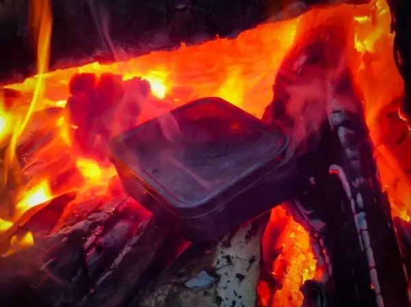 Ein Kochtopf steht auf glühenden Holzscheiten