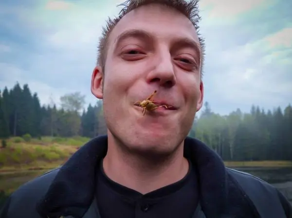 Ein Mann hält ein Insekt zwischen den Lippen und lächelt