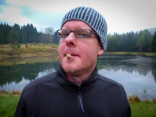 Ein Mann mit Brille und Mütze steht am Ufer eines Gewässers