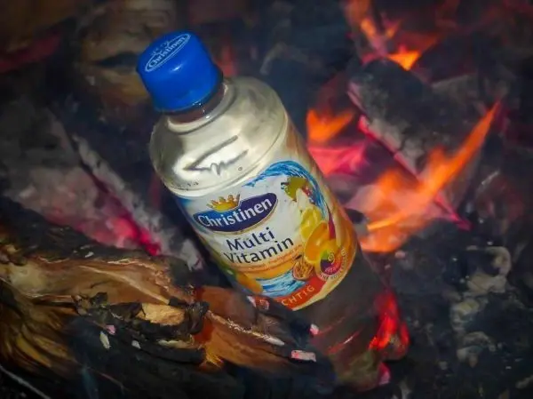 Flasche mit Getränk steht zwischen glühenden Holzscheiten und Flammen